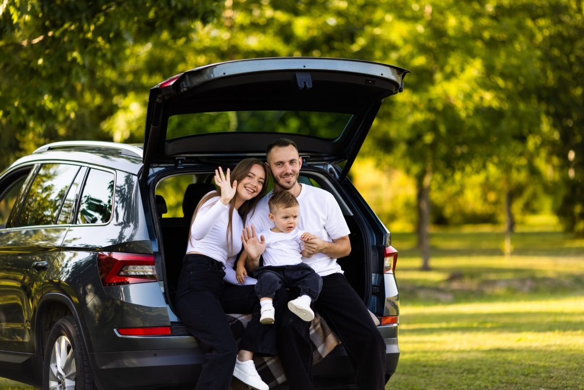 Young family with cute boy sitting in car trunk near forest